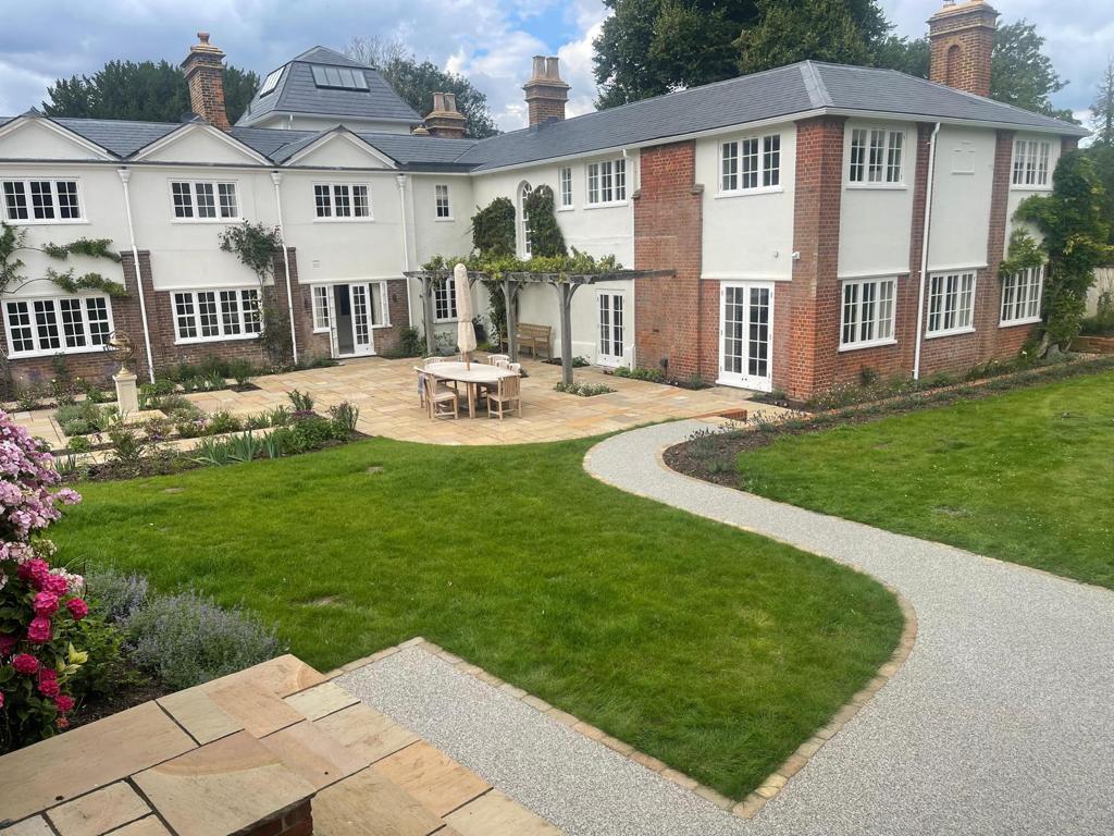 A large white house surrounded by a well-designed garden and lawn by Fost & Co.